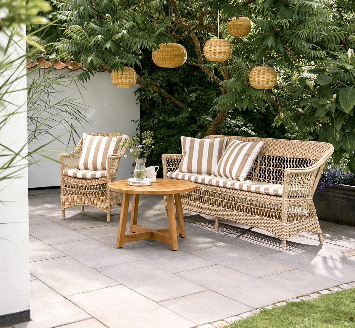 This is a lifestyle image of Charlot 3 Seater Sofa in natural ArtFibre Aluminium, on a coastal terrace with reed roof shade and sea views.