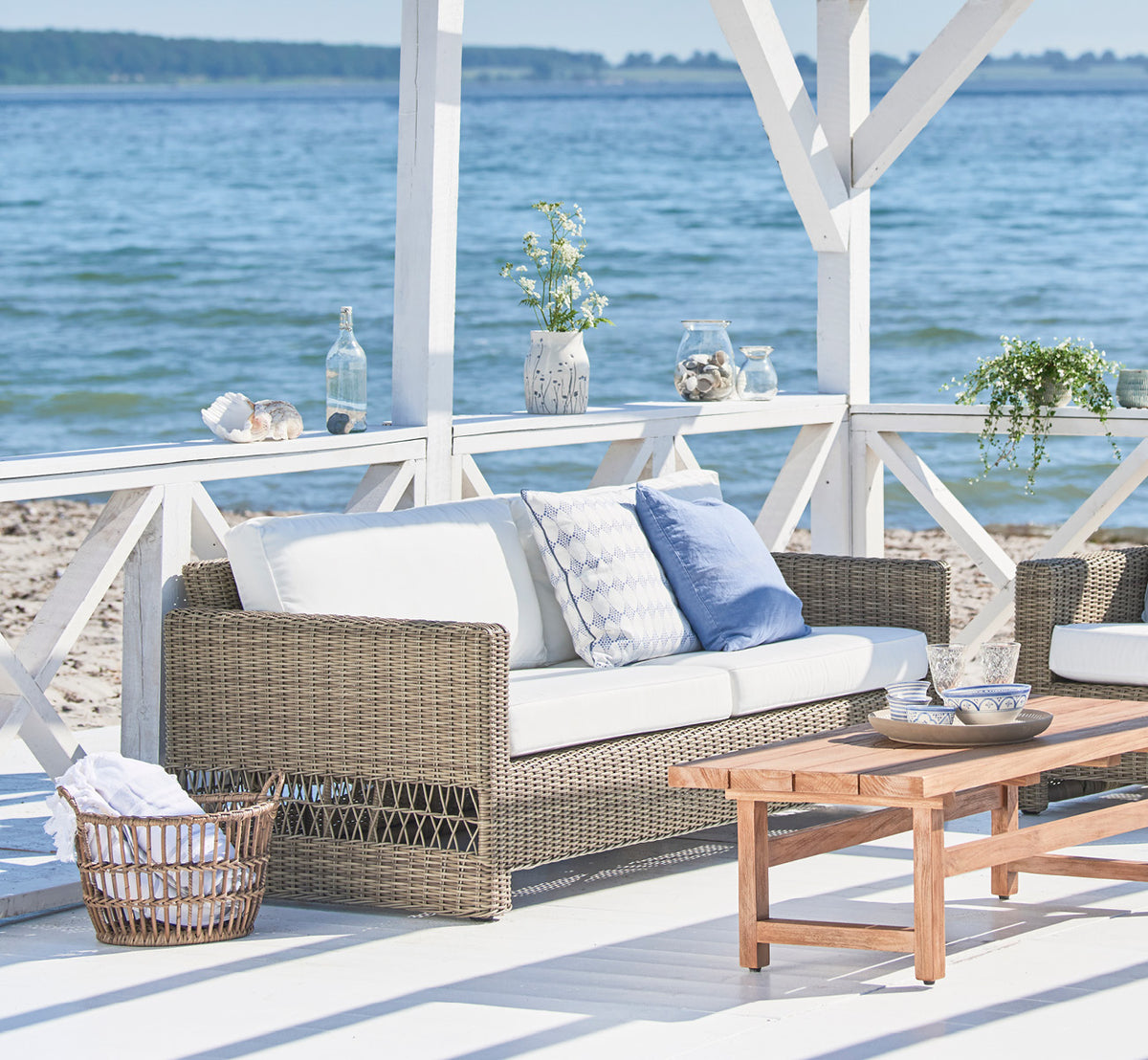 This is a lifestyle image of Carrie Sofa in antique Grey ArtFibre Aluminium, on a coastal terrace with white wooden deck, sea views and pergola.
