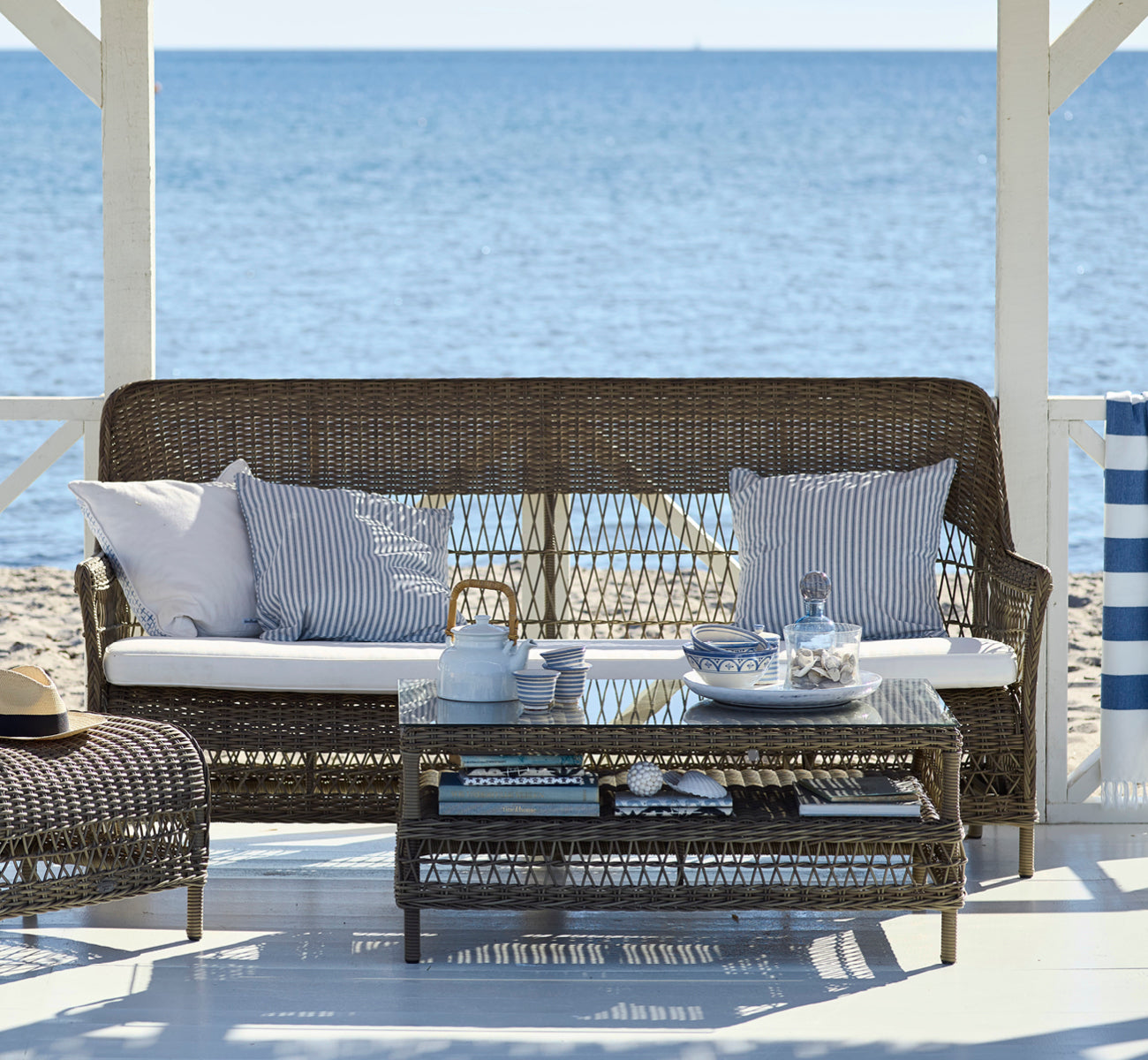 This is a lifestyle image of Dawn Sofa in antique Grey ArtFibre Aluminium, on a coastal terrace with white wooden decking and sea views.