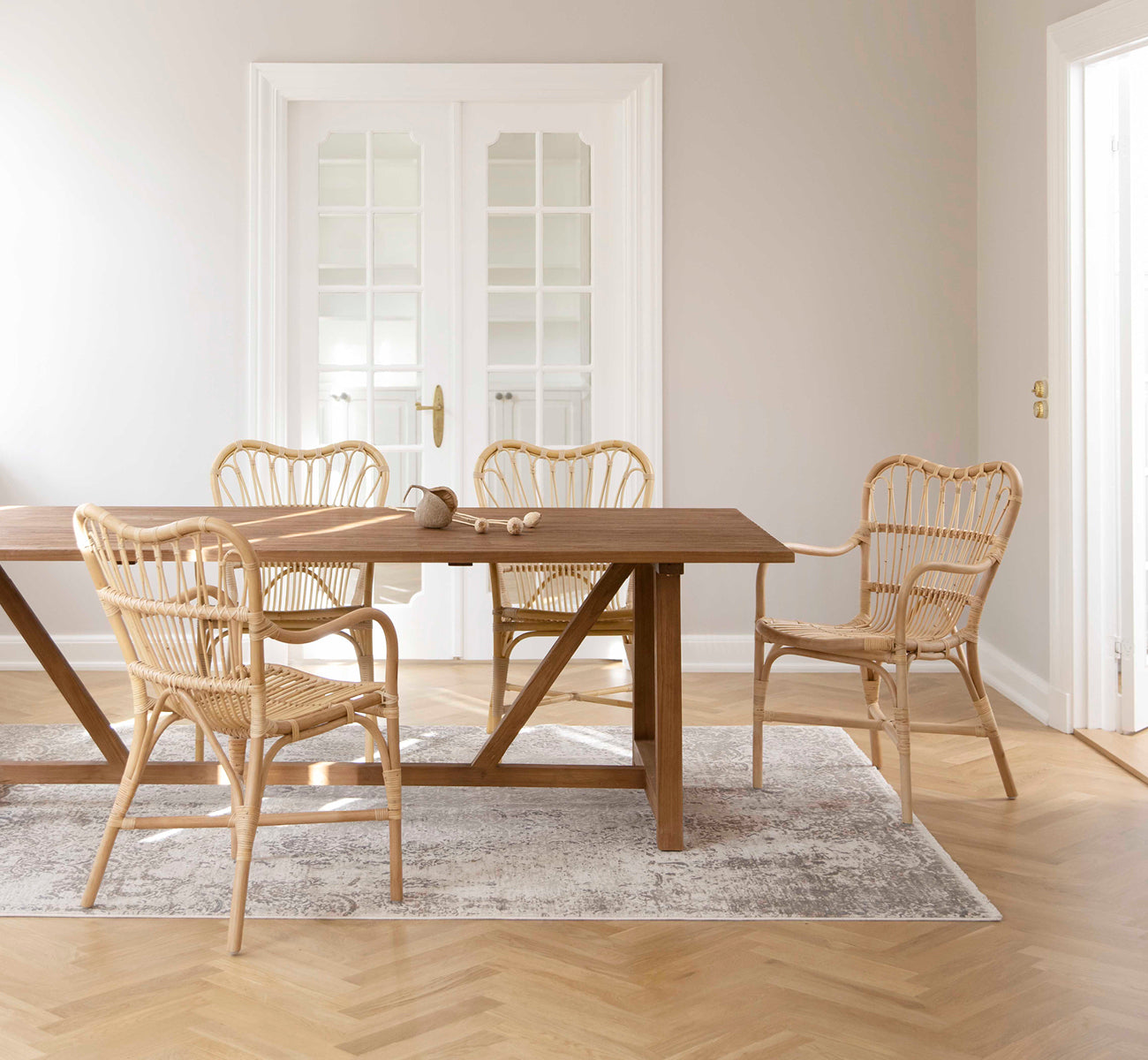 This is a lifestyle image of Lucas Teak Dining Table 240X100 cm in teak indoor. Set with rattan chairs in a bright room with herringbone oak floor.