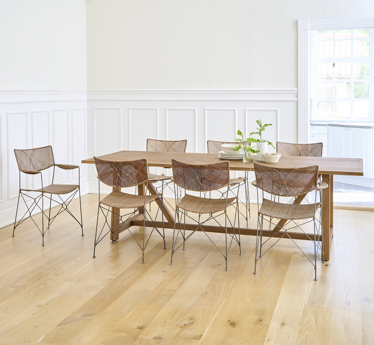 This is a lifestyle image of Lucas Teak Dining Table 240X100 cm in teak indoor. Paired with modern chairs in a bright room with white paneled walls.