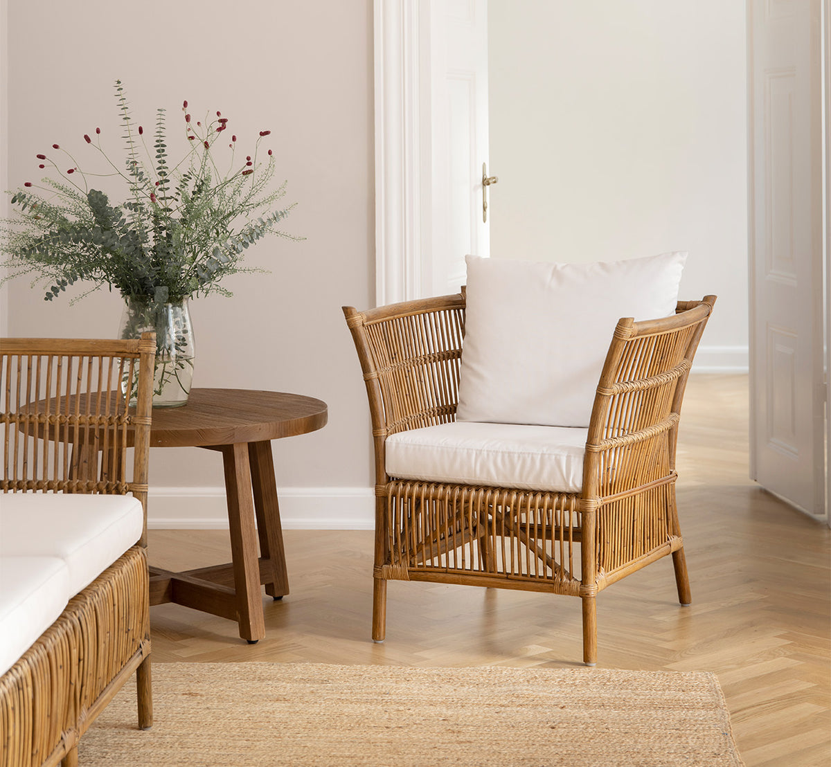 This is a lifestyle image of Aksel Coffee Table in teak indoor, in a bright interior with herringbone parquet and rattan chairs.