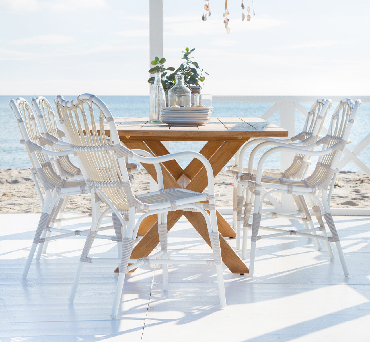 This is a lifestyle image of Colonial Table 160 in outdoor Teak, on a beachside terrace with white wooden decking and sea views.