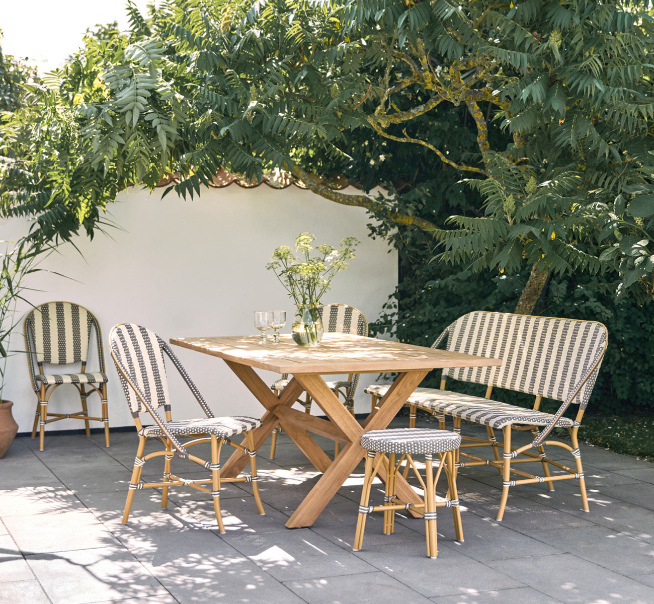 This is a lifestyle image of Colonial Table 160 in outdoor Teak, on a beachside terrace with white wooden decking and sea views.