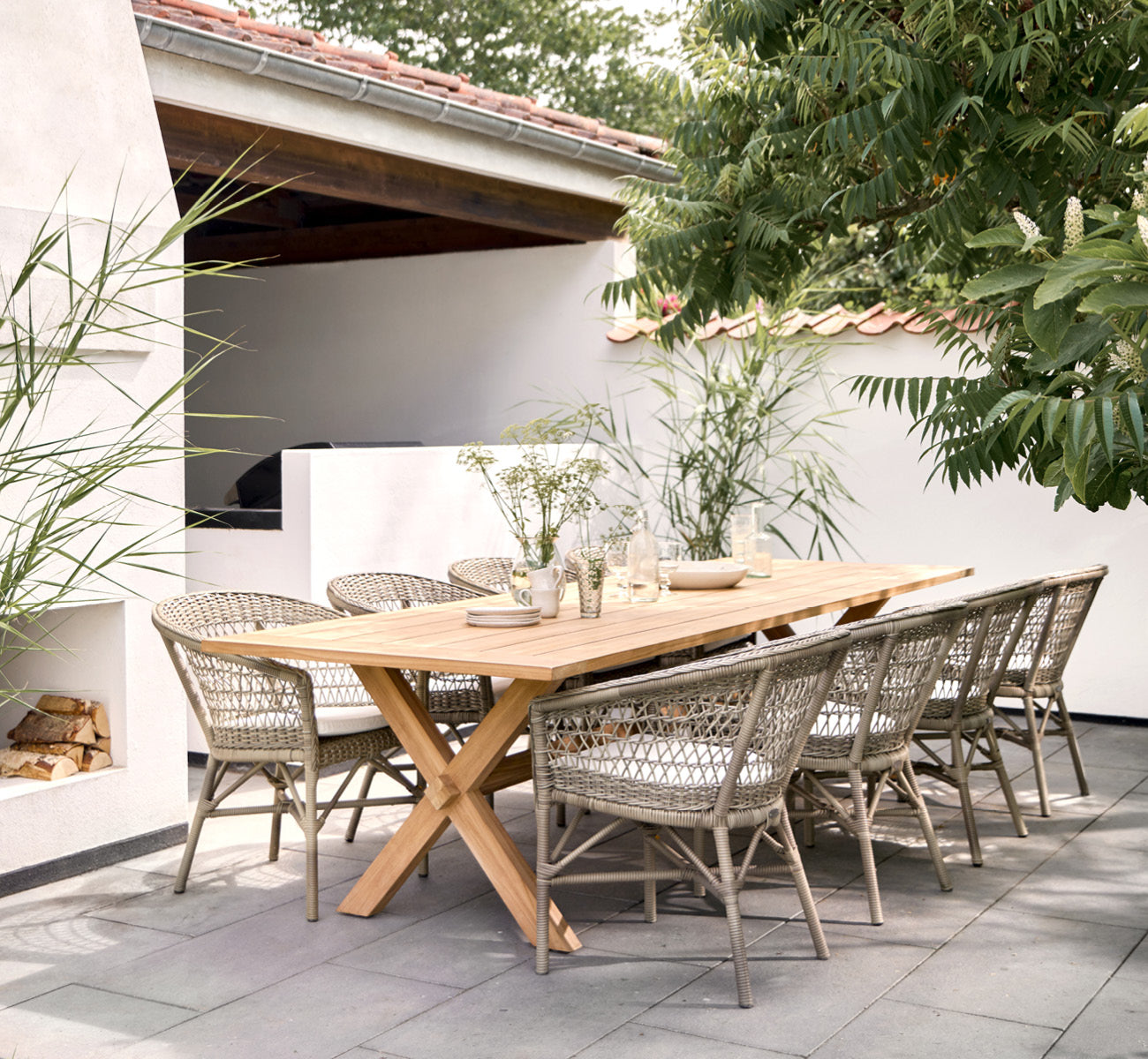 This is a lifestyle image of Colonial Table 300 in outdoor Teak, on a beachside terrace with white wooden decking and sea views.