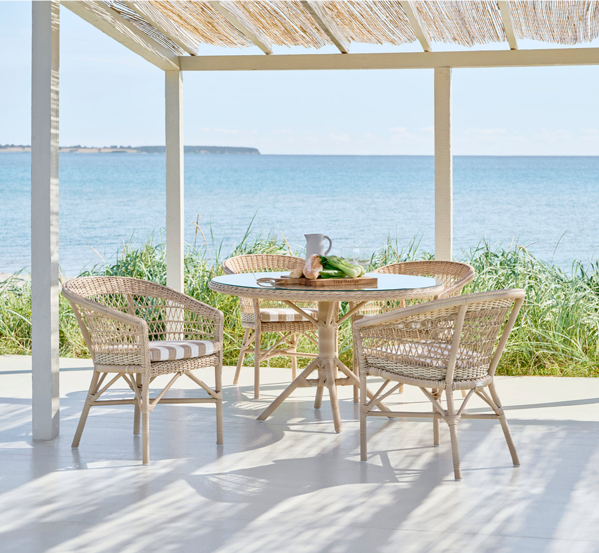 This is a lifestyle image of Grace Exterior Dining Table in natural ArtFibre Aluminium, in a lush garden patio with stone tile flooring and.
