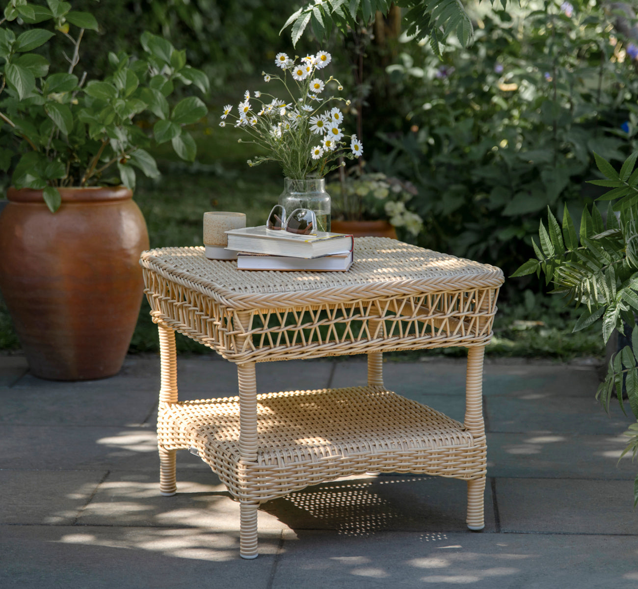 This is a lifestyle image of Susy Side Table in natural ArtFibre Aluminium, on a coastal terrace with sea views, beach grasses and white columns.