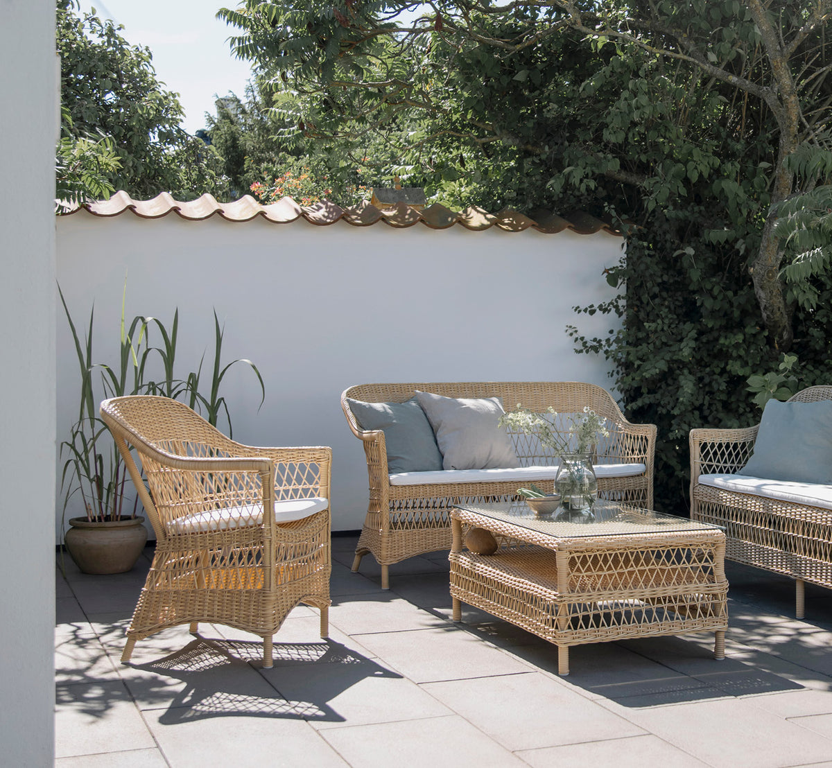 This is a lifestyle image of Hazel Coffee Table in natural ArtFibre Aluminium, on a shaded coastal terrace with reed canopy and sea views.