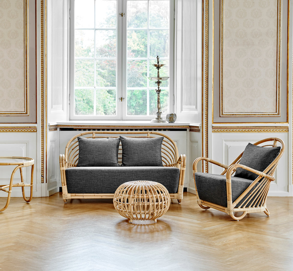 This is a lifestyle image of Charlottenborg Lounge Chair in polished Natural Rattan, in an elegant classical interior with ornate golden mouldings.