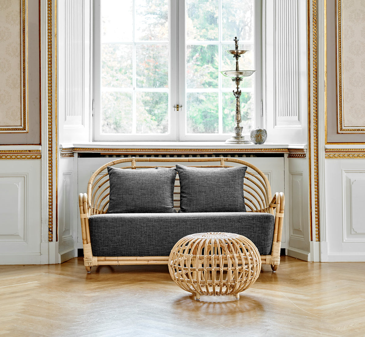 This is a lifestyle image of Charlottenborg Sofa in polished Natural Rattan, in an elegant classical interior with ornate golden mouldings.