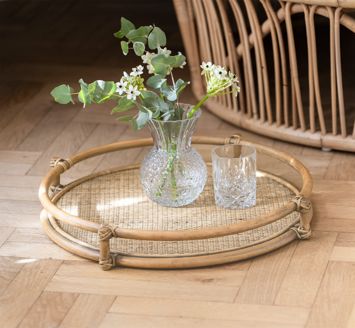 This is a lifestyle image of Andreas Tray in natural Rattan, in a bright interior with herringbone parquet flooring.
