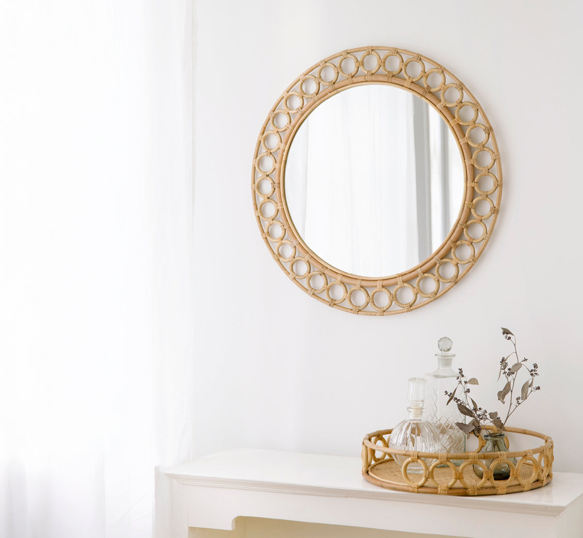 This is a lifestyle image of Mira Tray in natural rattan. Displayed with Mira Mirror on a white console with glass decanters.
