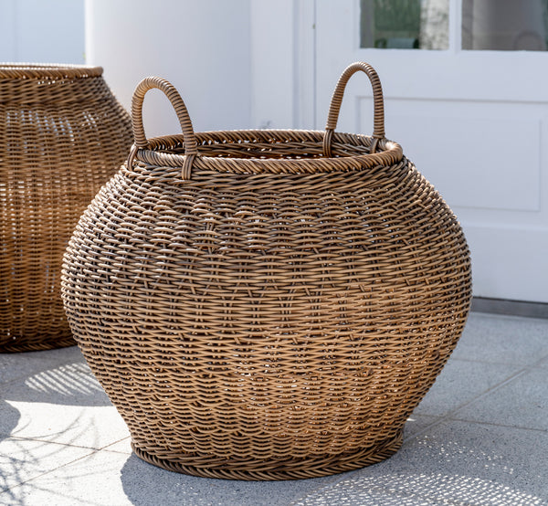 This is a lifestyle image of Smilla Basket in chestnut core weave ArtFibre Aluminium, outdoors on a sun-lit patio with a white wall and tile flooring.