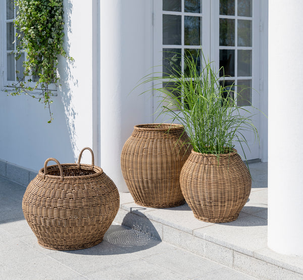 This is a lifestyle image of Ellis Basket in chestnut core weave ArtFibre Aluminium, outdoors on a sun-lit patio with a white wall and tile flooring.