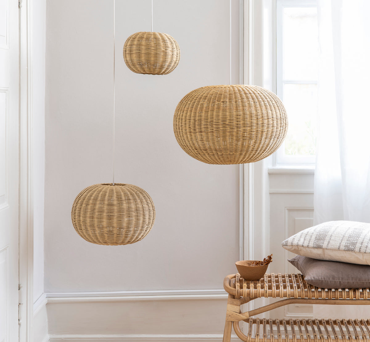 This is a lifestyle image of Tangelo Lampshade Ø37 cm | Small in natural rattan. Three pendants grouped above a rattan bench in a bright interior.