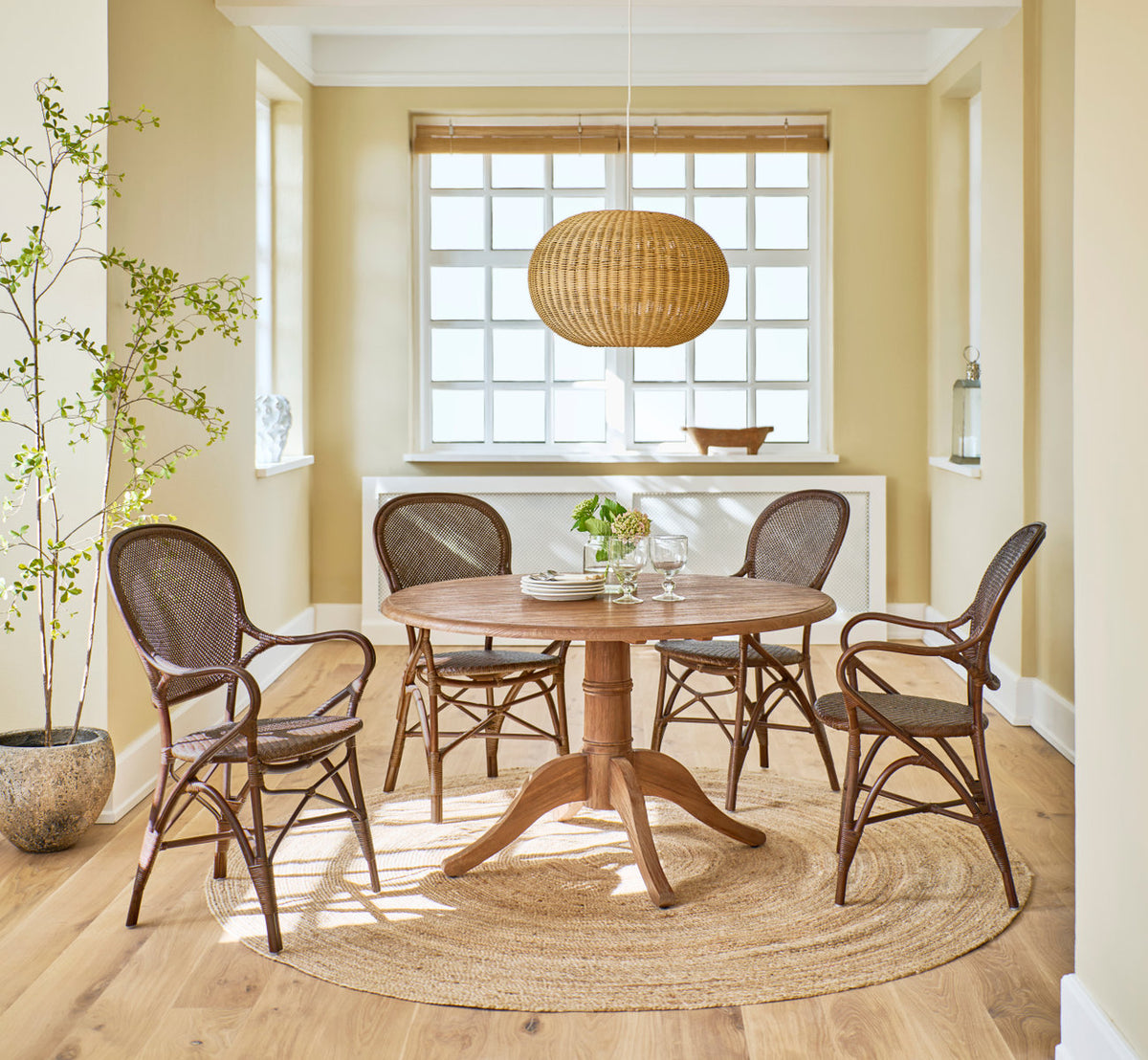 This is a lifestyle image of Tangelo Lampshade Ø49 cm-Medium in natural core weave iron frame. Above a round teak table with rattan chairs.