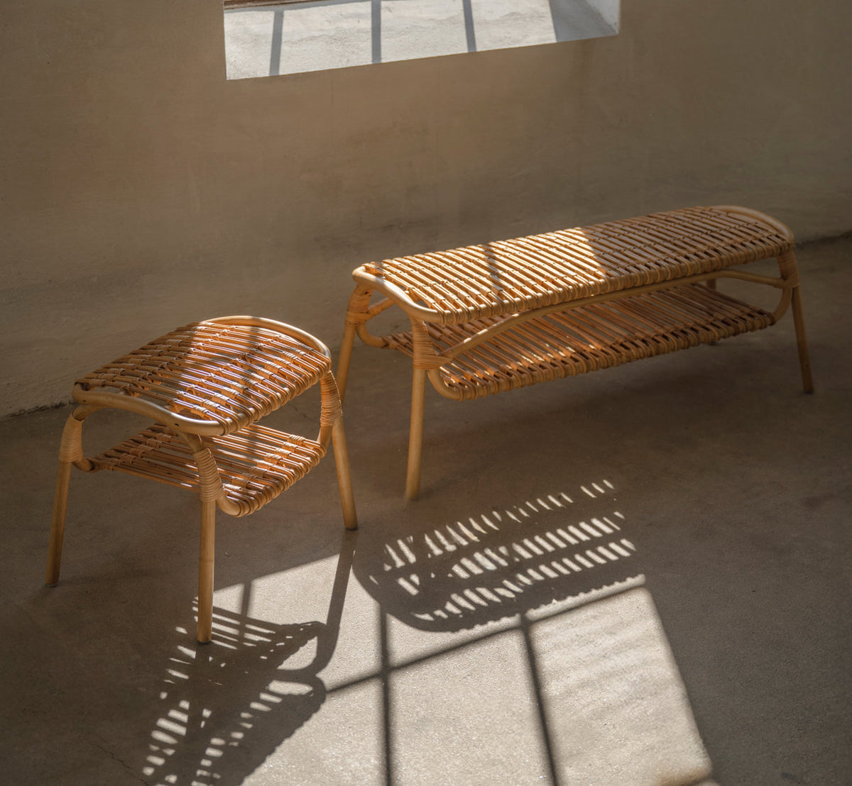 This is a lifestyle image of Machiya Bench in polished natural rattan. With stool casting striped shadows.