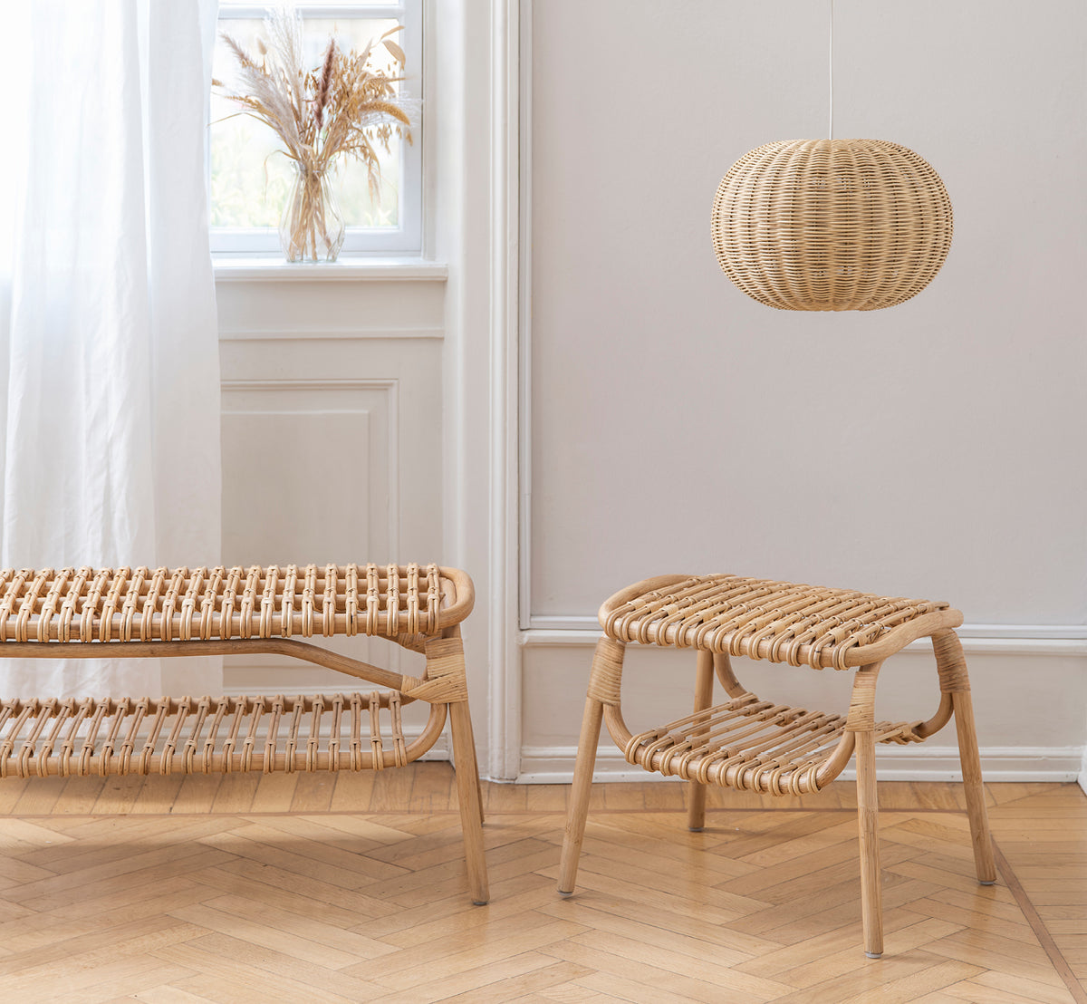 This is a lifestyle image of Machiya Bench in natural skin on rattan. Scandinavian room with a stool, pendant lamp, and pampas grass vase.