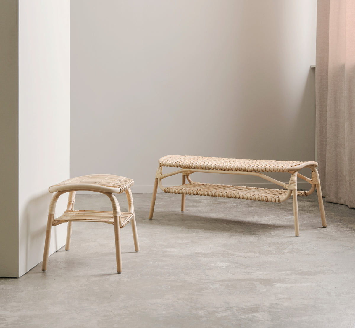 This is a lifestyle image of Machiya Bench in natural skin on rattan. Minimal room with concrete floor, rattan stool, and linen curtain.