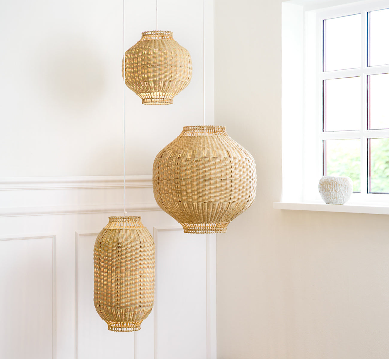 This is a lifestyle image of Tomori Lampshade in natural core weave rattan frame. The largest of three pendants in a bright paneled room.