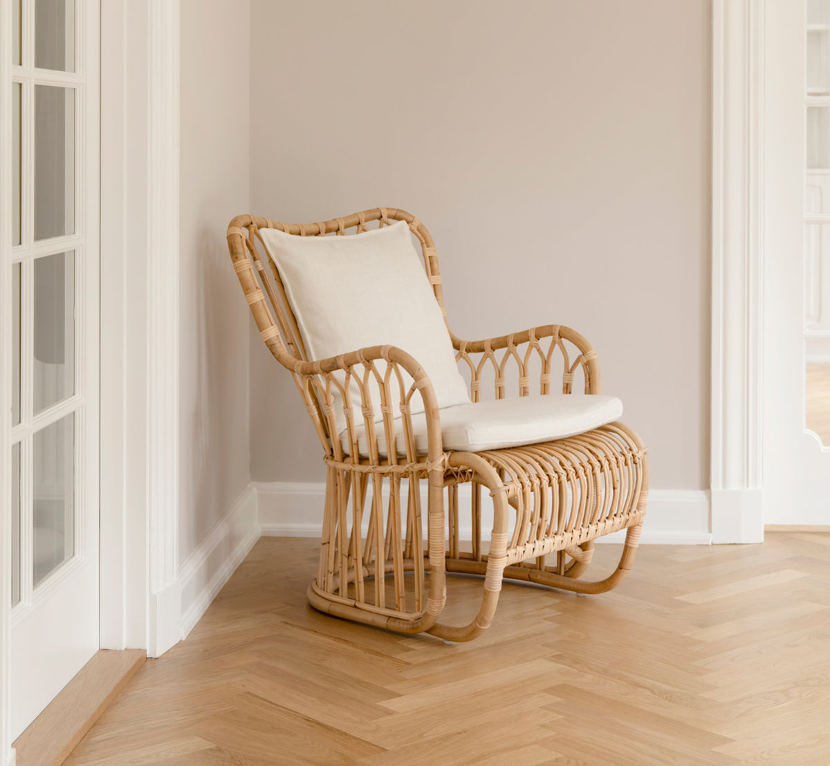 This is a lifestyle image of Tulip Lounge Chair in polished natural rattan. Paired with a matching sofa in a bright panelled room with door.