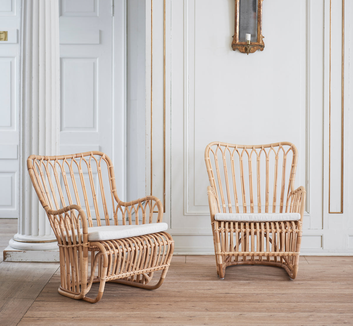 This is a lifestyle image of Tulip Lounge Chair in polished natural rattan. Paired with a matching sofa in a bright panelled room with door.