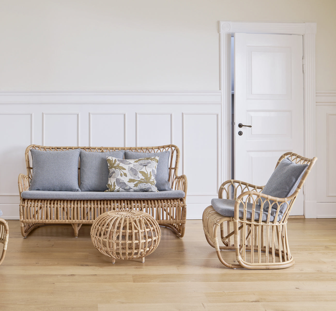 This is a lifestyle image of Tulip Sofa in polished natural rattan. Paired with a rattan lounge chair by a sunlit curtained window.