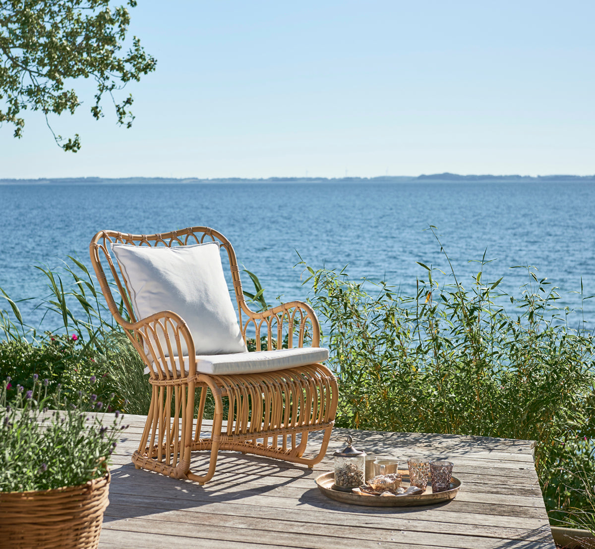 This is a lifestyle image of Tulip Exterior Lounge Chair in natural aluminium artfibre. Styled in a bright interior setting.