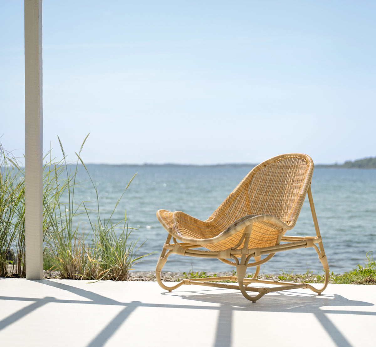This is a lifestyle image of Pacifique Exterior Lounge Chair in natural core weave artfibre aluminium. Styled in a bright interior setting.