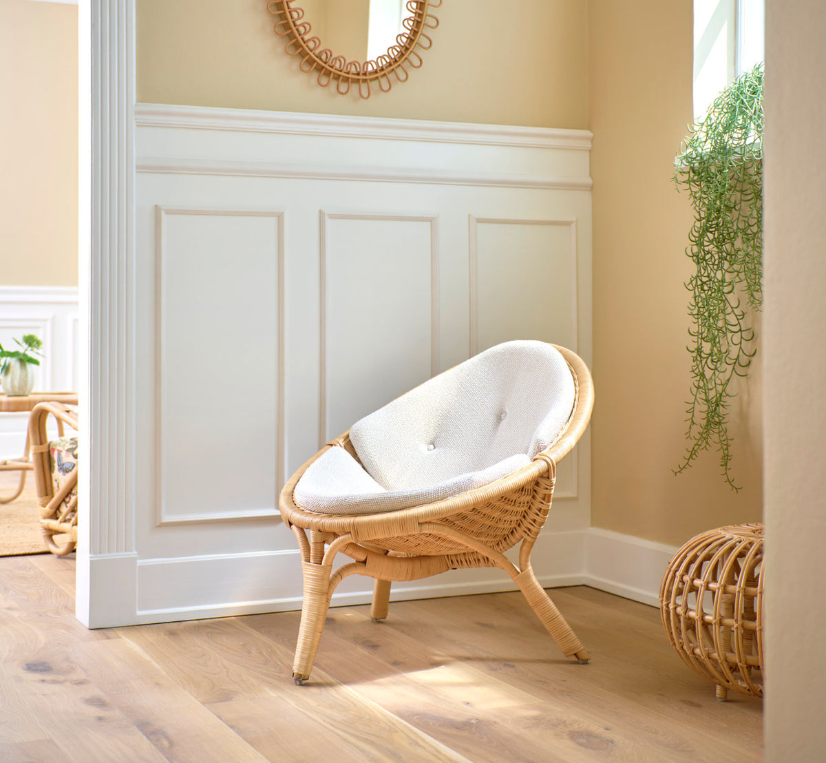 This is a lifestyle image of Rana Lounge Chair in natural core weave rattan frame. With white cushion by panels and a plant.