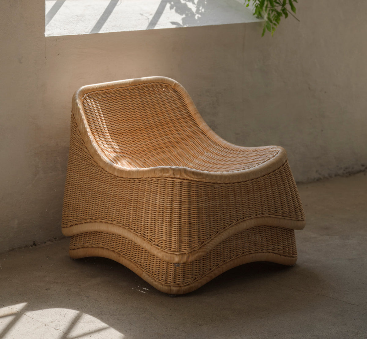 This is a lifestyle image of Chill Lounge Chair in natural core weave rattan frame. In warm sunlight against a pale wall.