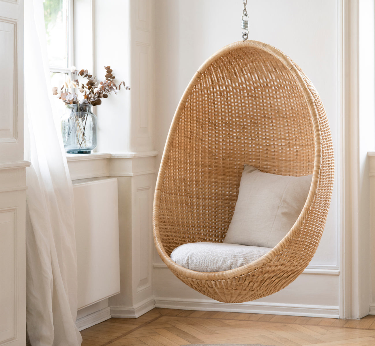 This is a lifestyle image of Hanging Egg Chair in natural core weave Rattan frame, in an elegant classical interior with ornate golden mouldings.