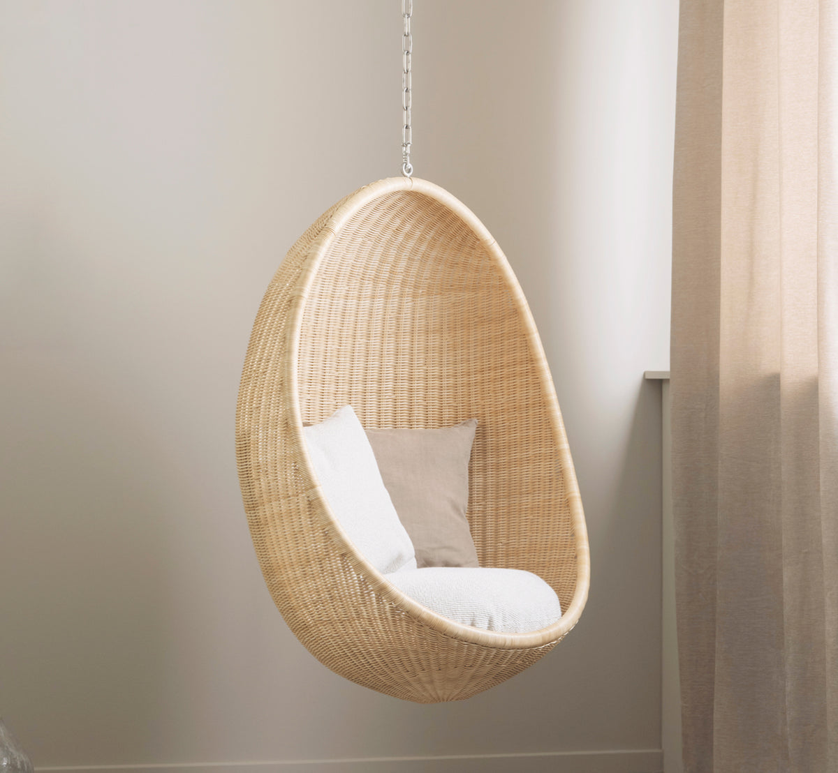 This is a lifestyle image of Hanging Egg Chair in natural core weave Rattan frame, in an elegant classical interior with ornate golden mouldings.