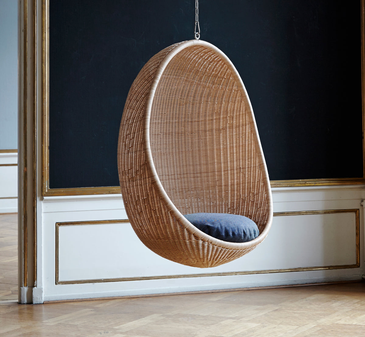 This is a lifestyle image of Hanging Egg Chair in natural core weave Rattan frame, in an elegant classical interior with ornate golden mouldings.