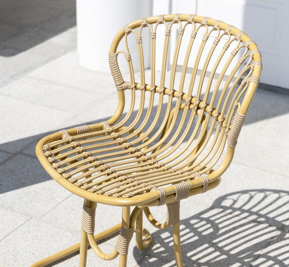 This is a lifestyle image of Rita Exterior Dining Chair in natural aluminium artfibre. Paired with a bistro table on a white colonnaded terrace.