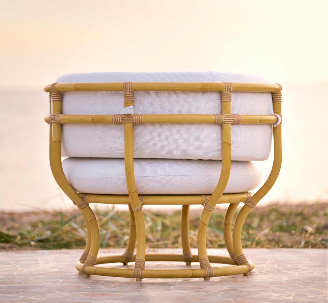 This is a lifestyle image of Coco Exterior Lounge Chair in natural Aluminium ArtFibre, on an open coastal terrace at sunset with sea views.