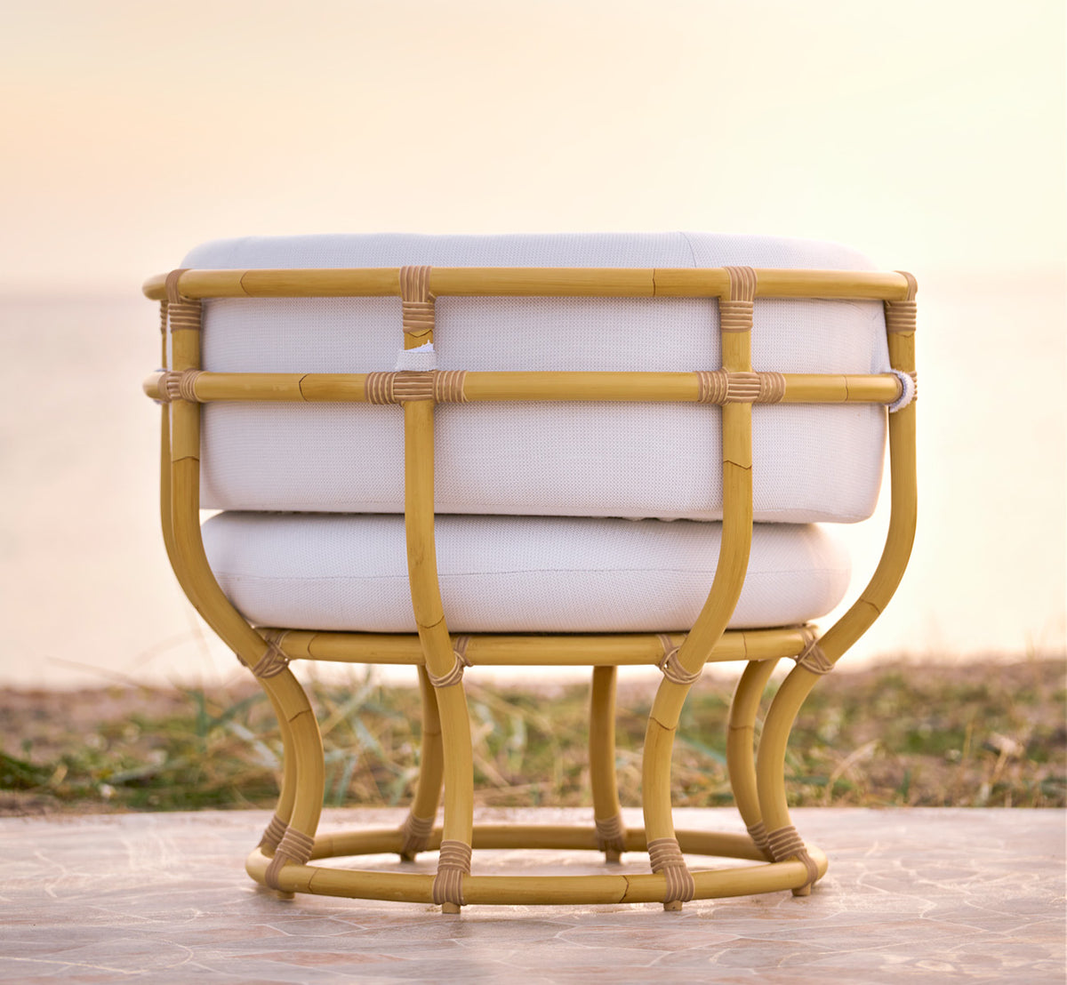 This is a lifestyle image of Coco Exterior Lounge Chair in natural Aluminium ArtFibre, on an open coastal terrace at sunset with sea views.