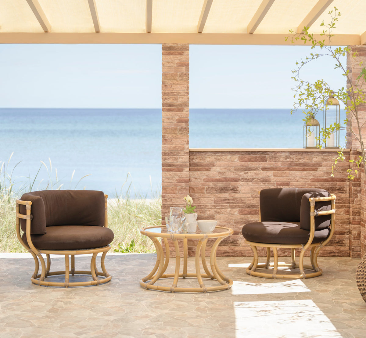 This is a lifestyle image of Coco Exterior Lounge Chair in natural aluminium artfibre. Lounge chairs and table on a seaside terrace.
