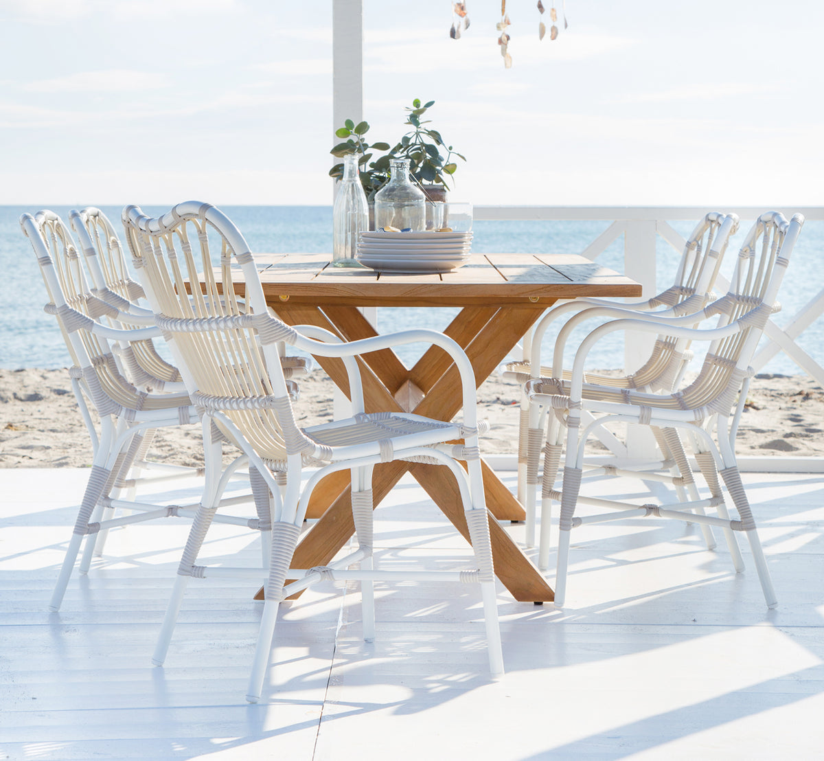 This is a lifestyle image of Margret Exterior Dining Armchair in dove white aluminium artfibre. Beach terrace with teak table and decorations.