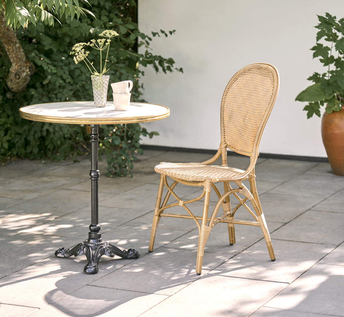 This is a lifestyle image of Rossini Exterior Dining Chair in antique aluminium artfibre. Styled in a bright interior setting.
