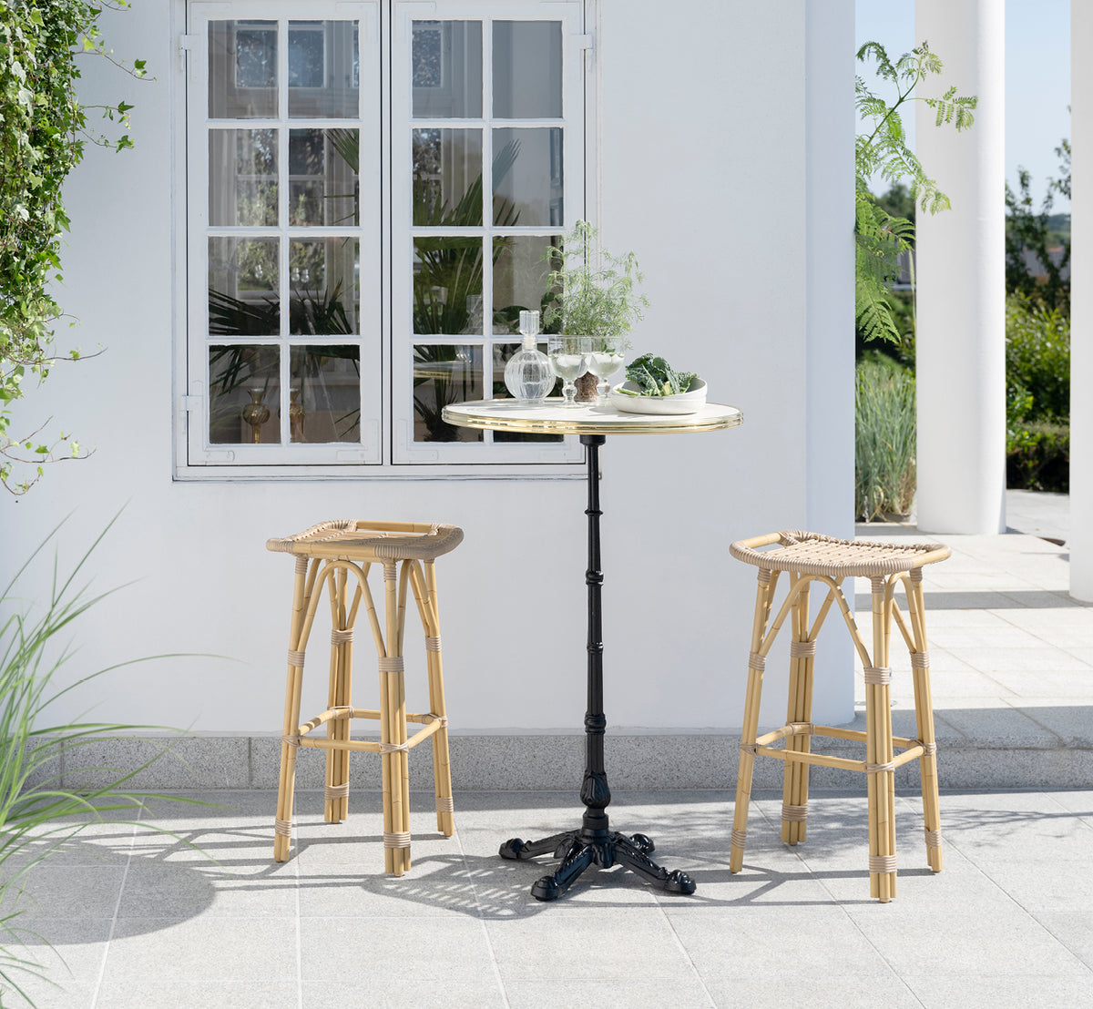 This is a lifestyle image of Salsa Exterior Bar Stool in natural aluminium artfibre. Elegant patio with bar table and green plants.