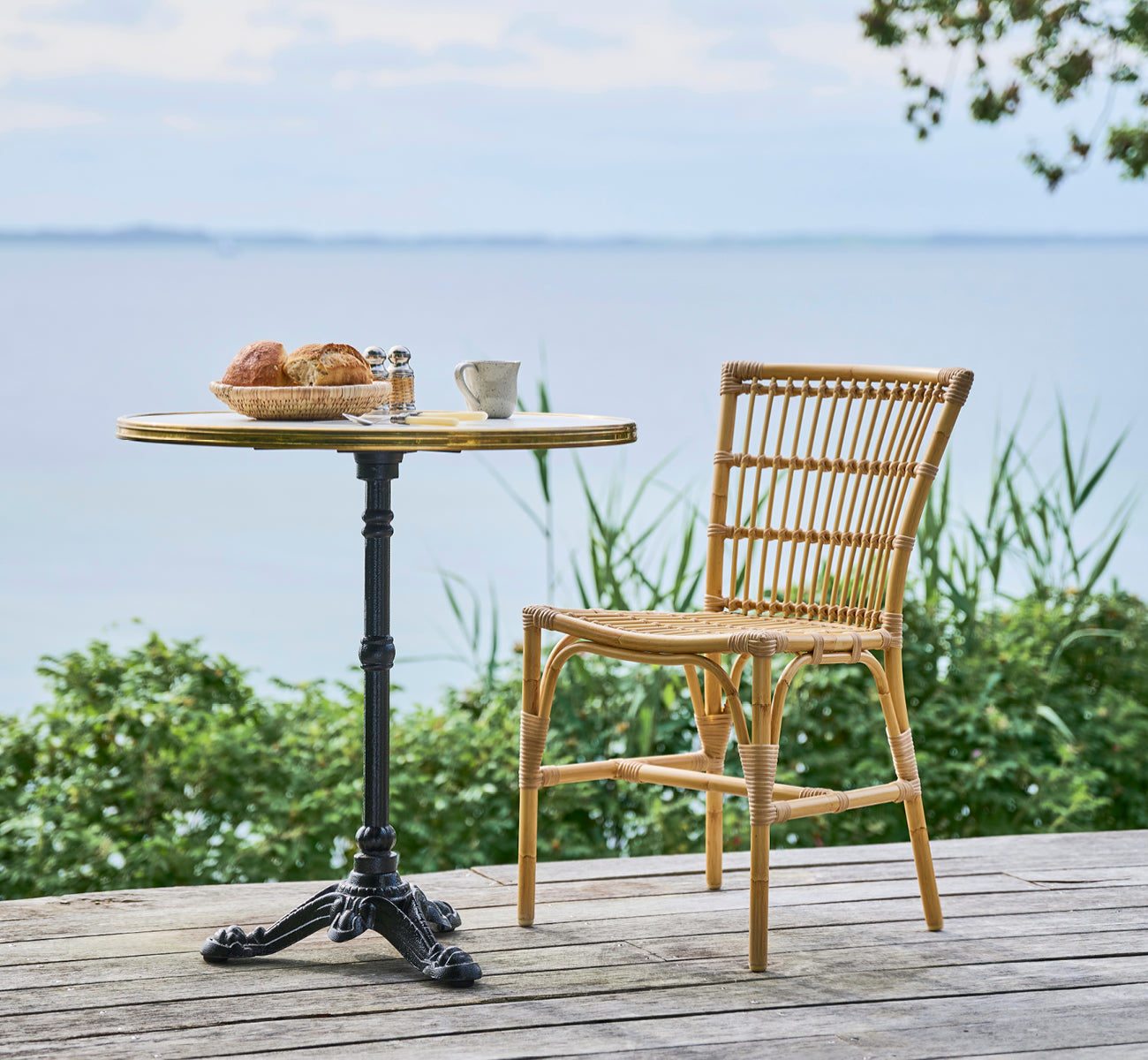 This is a lifestyle image of Elisabeth Exterior Dining Chair in natural Aluminium ArtFibre, on a wooden deck with a bistro breakfast table.