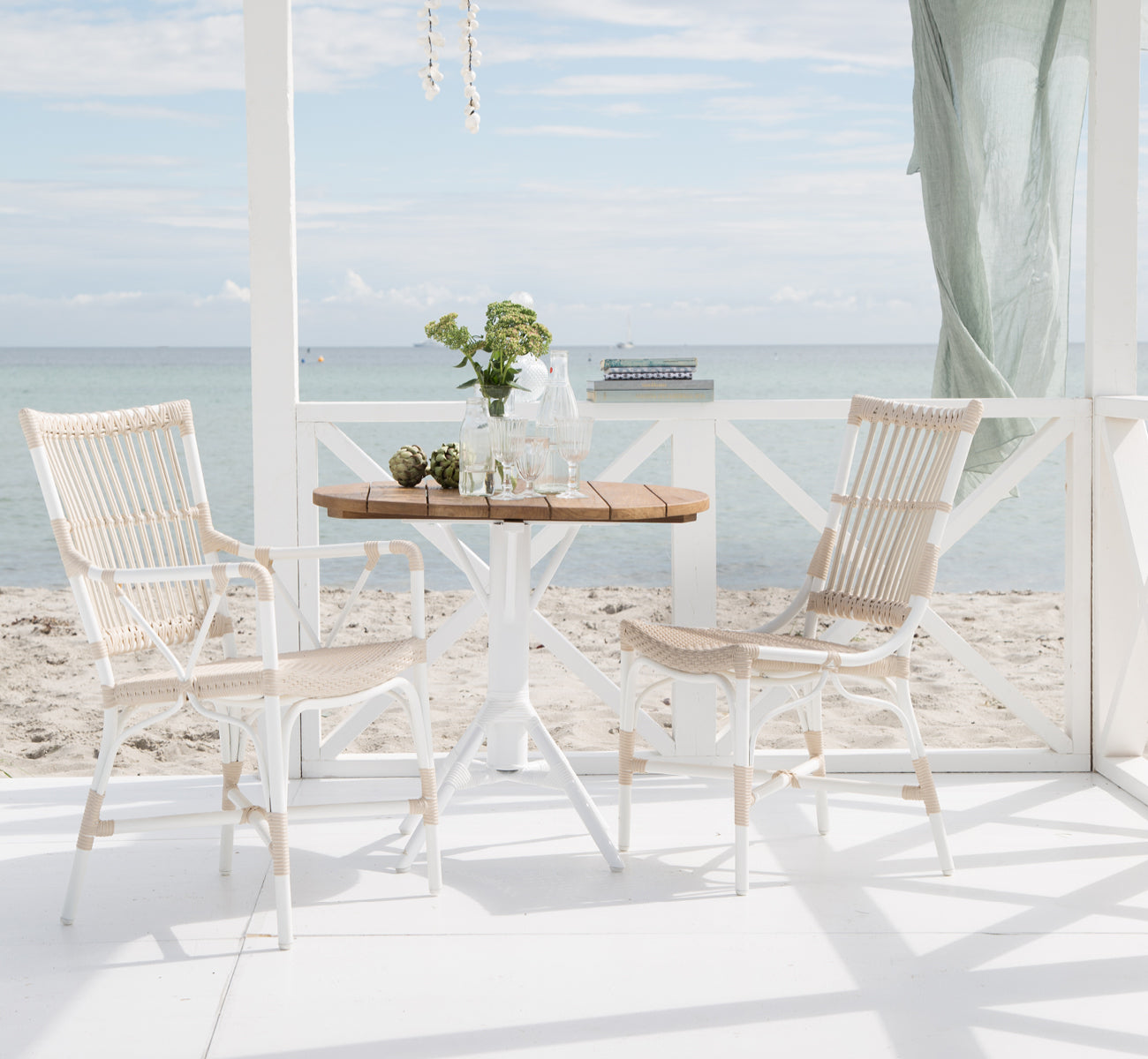 This is a lifestyle image of Piano Exterior Dining Armchair in dove white aluminium artfibre. At a seaside pergola with ocean view.