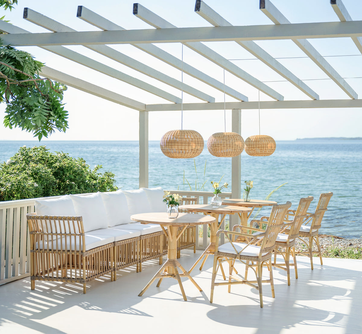 This is a lifestyle image of Piano Exterior Dining Armchair in natural aluminium artfibre. On a seaside pergola with rattan pendants.