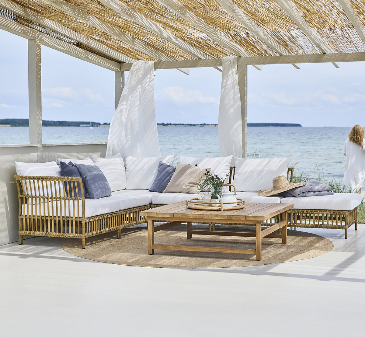 This is a lifestyle image of Maggie Sofa Center Module in antique aluminium artfibre. Beach pavilion with modular sofa and ocean view.