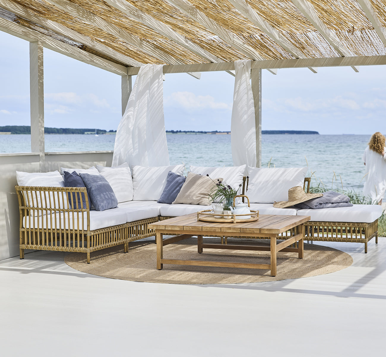 This is a lifestyle image of Maggie Sofa Center Module in antique aluminium artfibre. Beach pavilion with modular sofa and ocean view.
