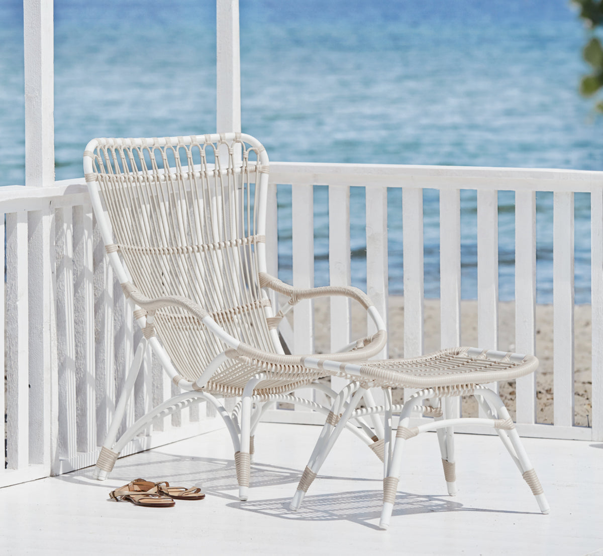 This is a lifestyle image of Monet Exterior Lounge Chair in dove white aluminium artfibre. With footstool on a seaside porch.