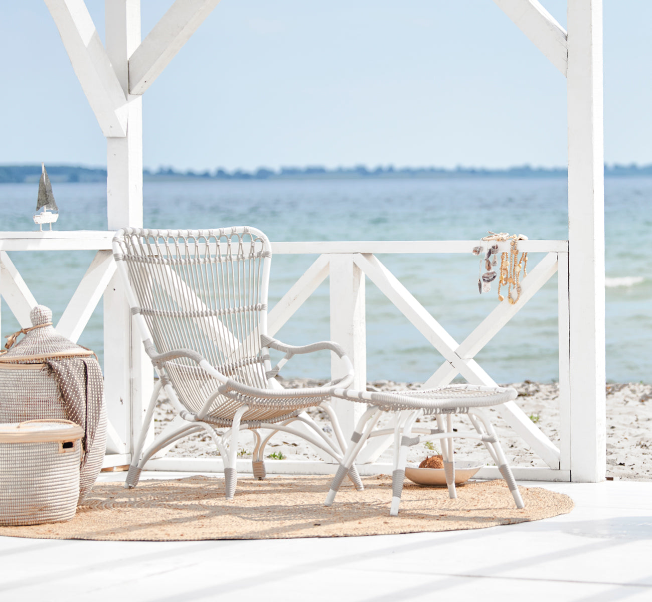 This is a lifestyle image of Monet Exterior Lounge Chair in dove white aluminium artfibre. On a beach pavilion with jute rug.