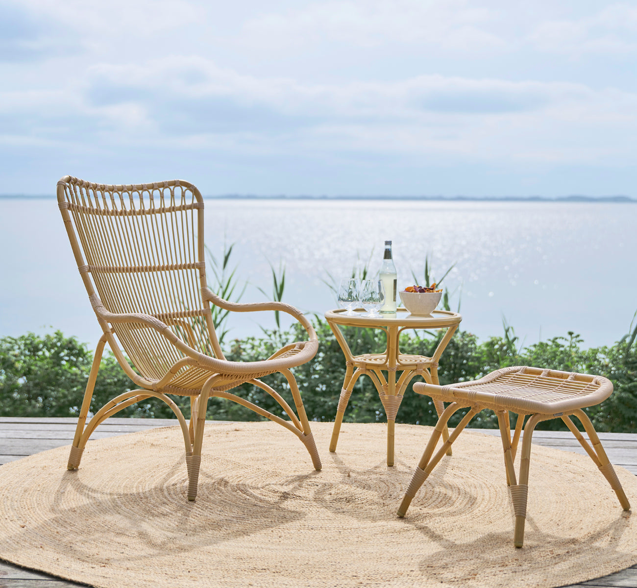 This is a lifestyle image of Monet Exterior Lounge Chair in natural aluminium artfibre. With footstool on a deck overlooking the sea.