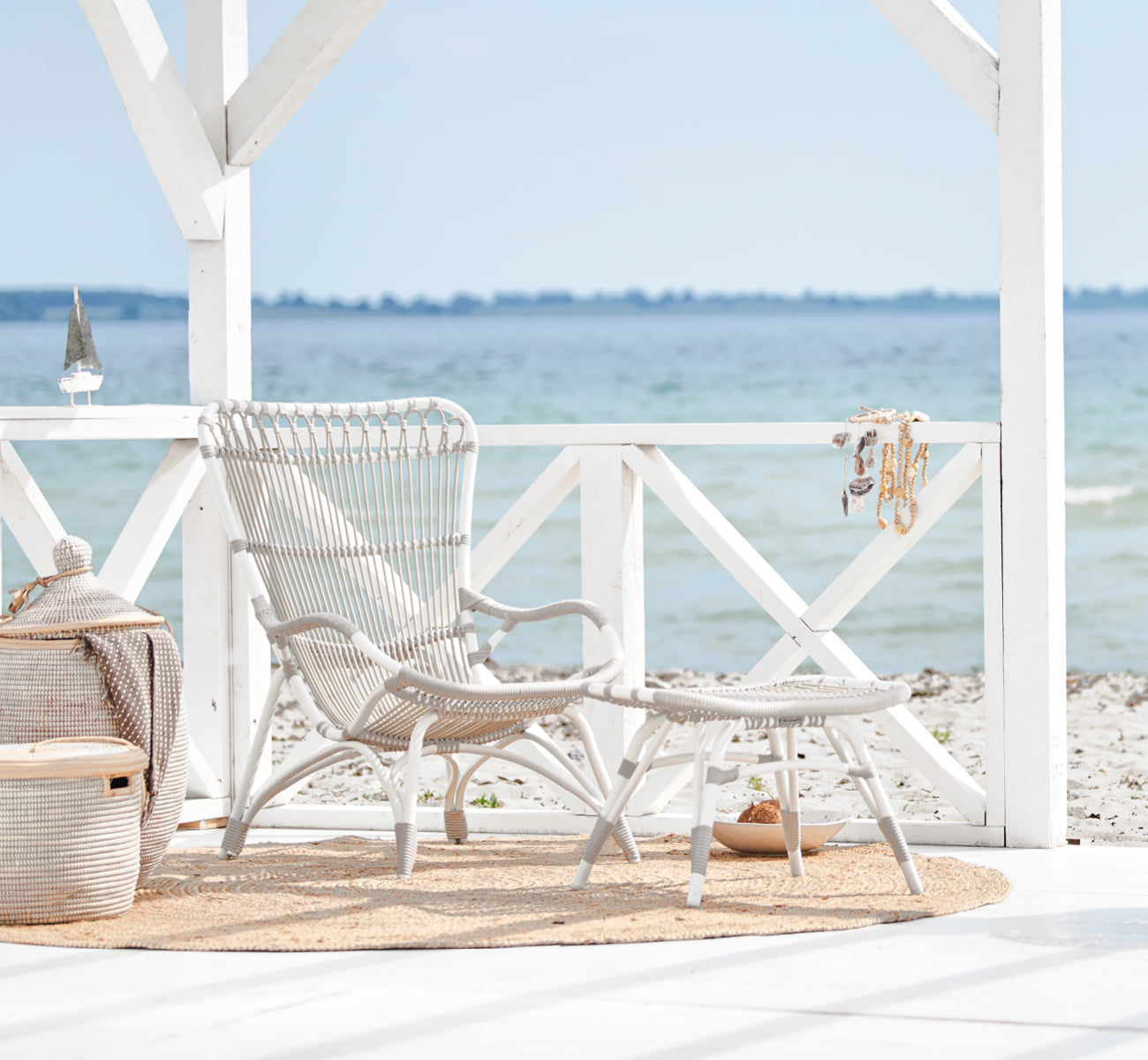 This is a lifestyle image of Monet Exterior Footstool in dove white aluminium artfibre. On a beach pavilion with jute rug and basket.